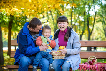 Fototapeta premium happy family enjoying autumn picnic. Father mother and son sit on bench with apples basket. Happy family leisure together concept