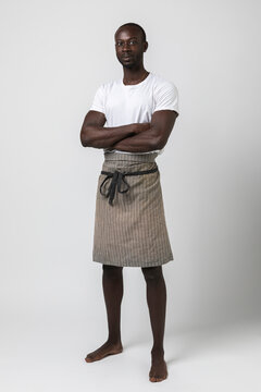 African boy with apron poses three-quarter on white background in photo studio. Full body portrait.