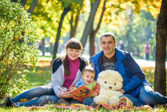 happy family enjoying autumn picnic. Father mother and son sit on field with apples basket teddy bear and reading book. Happy family leisure together concept