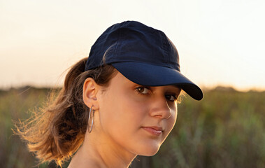 Teen girl in dark blue baseball cap at sunset