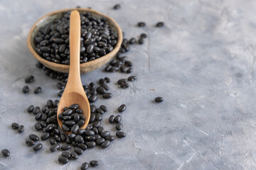 Bowl full of dried black beans with a wooden spoon on grey table