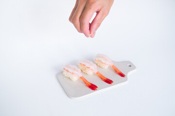 Raw Shrimp prawn sushi in japanese restaurant. Sushi - ama Ebi Nigiri on white board on white background. The chef pours salt. High quality photo 