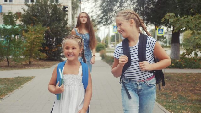 group of schoolchildren walking to school along the path. happy family school concept.little schoolgirl with backpack and textbook. schoolgirls walk along in the park education to school for lessons - Powered by Adobe
