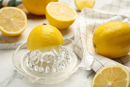 Glass squeezer and fresh lemons on white marble table