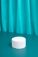 Podiums or pedestal Mock-up for cosmetic production on a turquoise background with folds of fabric.
