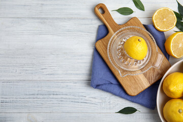 Glass squeezer and fresh lemons on white wooden table, flat lay. Space for text