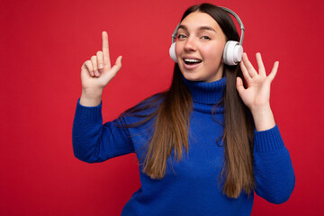Attractive positive young brunette woman wearing blue sweater isolated over red background wall...