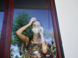 Fototapeta premium woman in the window wearing a medical mask ban quarantine