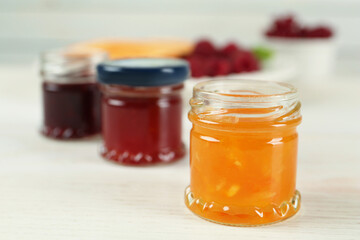 Jars with different sweet jams on white wooden table, closeup. Space for text