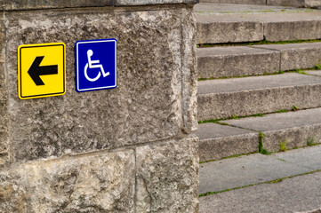 signs at the stone staircase indicating the direction to the ramp for persons with disabilities