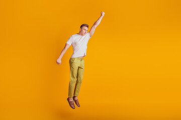 Fototapeta na wymiar Portrait of crazy superhero guy jump raise fist fly on yellow background