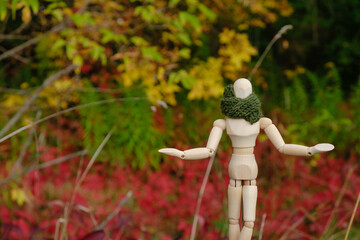 Human wooden figure in a green scarf on the autumn background. The wooden mannequin raised his hands. Copy space. 
