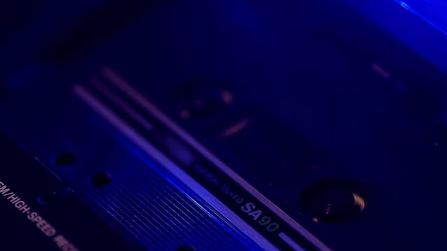 Portative studio rolls vintage audio cassette in neon light