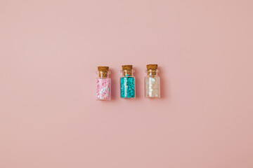 Three glass bottles with pink and blue glitter sequins on a pastel pink background. Christmas, holiday and party backdrop. Copy space.