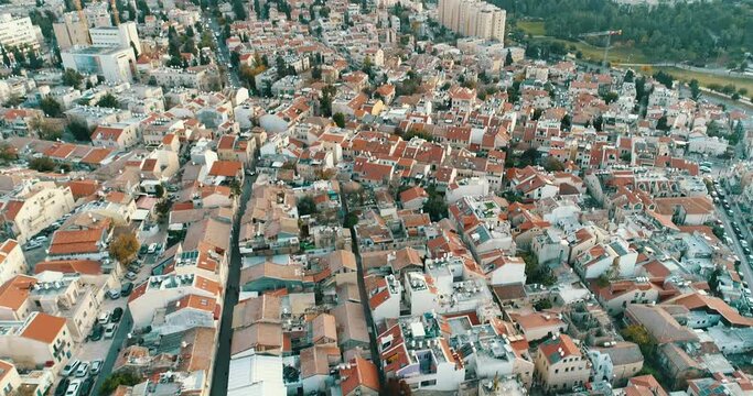 Aerial View of Jerusalem, Israel, Old Residential Buildings with Red Roofs and Small Streets at Evening, Revealing Newer Tall Buildings While Gently Tilting up from Birds Eye View Towards Horizon.