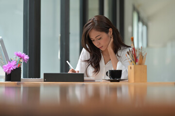 Photo of a young designer drawing on a digital tablet with a stylus pen at the wooden working desk.