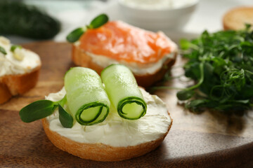 Delicious sandwiches with cream cheese and other ingredients on wooden board, closeup