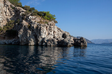Naklejka premium Mediterranean rocky shores with green trees and landscape. View from sea. Rock reflection in blue water sea.