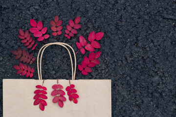 Shopping bag with red leaves on the asphalt background with top view. Still life for autumn sales. Seasonal buying and selling for females. Autumn bright backdrop.