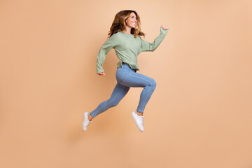 Fototapeta na wymiar Full length body size photo woman jumping high running cheerful happy casual clothes isolated pastel beige color background
