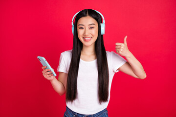 Photo of young asian girl happy positive smile listen music use cellphone show thumb-up isolated over red color background