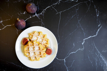 on a white round plate with pieces of figs and cinnamon sticks on a black marble table are two Belgian waffles made of corn flour, eggs and pumpkin. top view . gluten-free homemade food