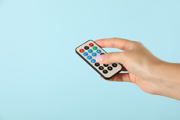 Woman holding remote control on light blue background, closeup. Space for text