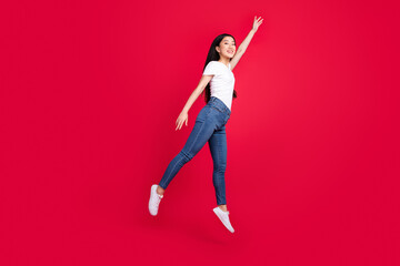 Photo of dreamy energetic sportive korean lady jump wear white t-shirt jeans sneakers isolated red color background