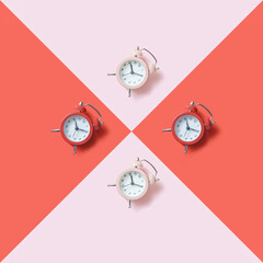 Creative flat lay composition with four retro alarm clocks on geometric duo tone red and pink background.