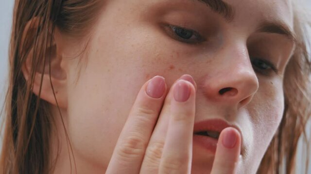 Closeup of attractive female young face with freckles. Young woman applying creme massaging facial skin with nourishing lotion. Concept for health, skincare and wellness.