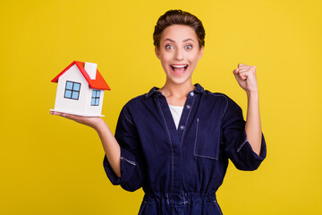 Fototapeta na wymiar Portrait of young excited crazy smiling girl raise fist in success moving new home relocation isolated on yellow color background