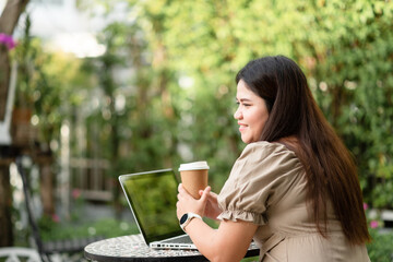 Rear view of Asian woman is using her laptop to check email and work via the internet with a coffee next to her ,Working from home concept.