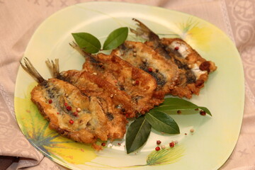 Crispy deep fried small fish on a plate, decorated with bay leaves and spices. Dough herring. Herring recipes