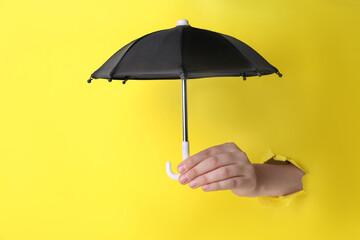 Woman holding open small black umbrella through hole in yellow paper, closeup