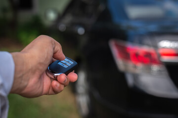 Hand of a man holding and push remote control of black car, technology transportation safety concept