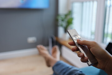 Woman is sitting on sofa and holding TV remote control in her hands closeup