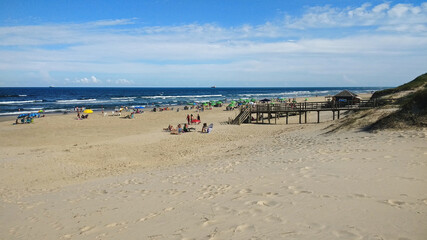 People go to the beach on a sunny day with clear sand and vivid blue in the ocean. Imbé, southern Brazil.