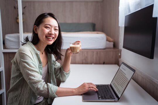Smiling Asian writer with laptop and coffee at home