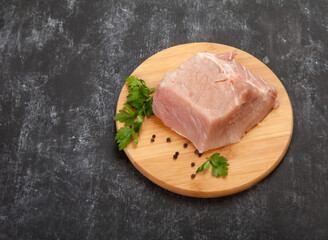 A piece of raw meat with herbs lies on a wooden cutting board on a black background.