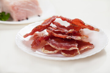 Jerky in a cup and raw meat with herbs on a white plate.