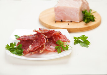 Jerky in a cup and raw meat with herbs on a white plate.