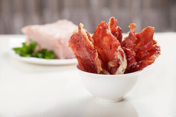 Jerky in a cup and raw meat with herbs on a white plate.