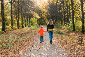 Fototapeta premium Mother and son walking in the fall park and enjoying the beautiful autumn nature. Season, single parent and children concept.