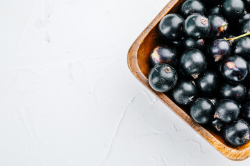 Black currant on a wooden board on a white concrete table