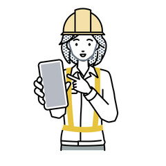 立ってスマートフォンを指差してこちらに向けて見せている工事現場の女性
