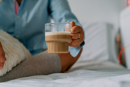 Crop woman with aromatic latte on bed