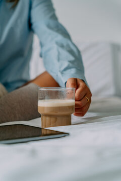 Crop woman with aromatic latte on bed