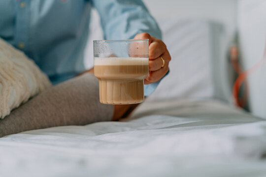 Crop woman with aromatic latte on bed