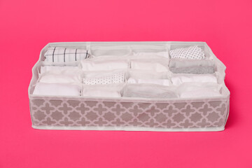 Textile organizer with folded clothes on pink background