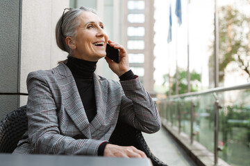 Grey white senior woman talking on cellphone while sitting in cafe